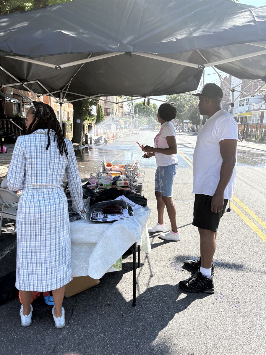 Neighbors at the supply tables under the canopy, the closed street running away behind them