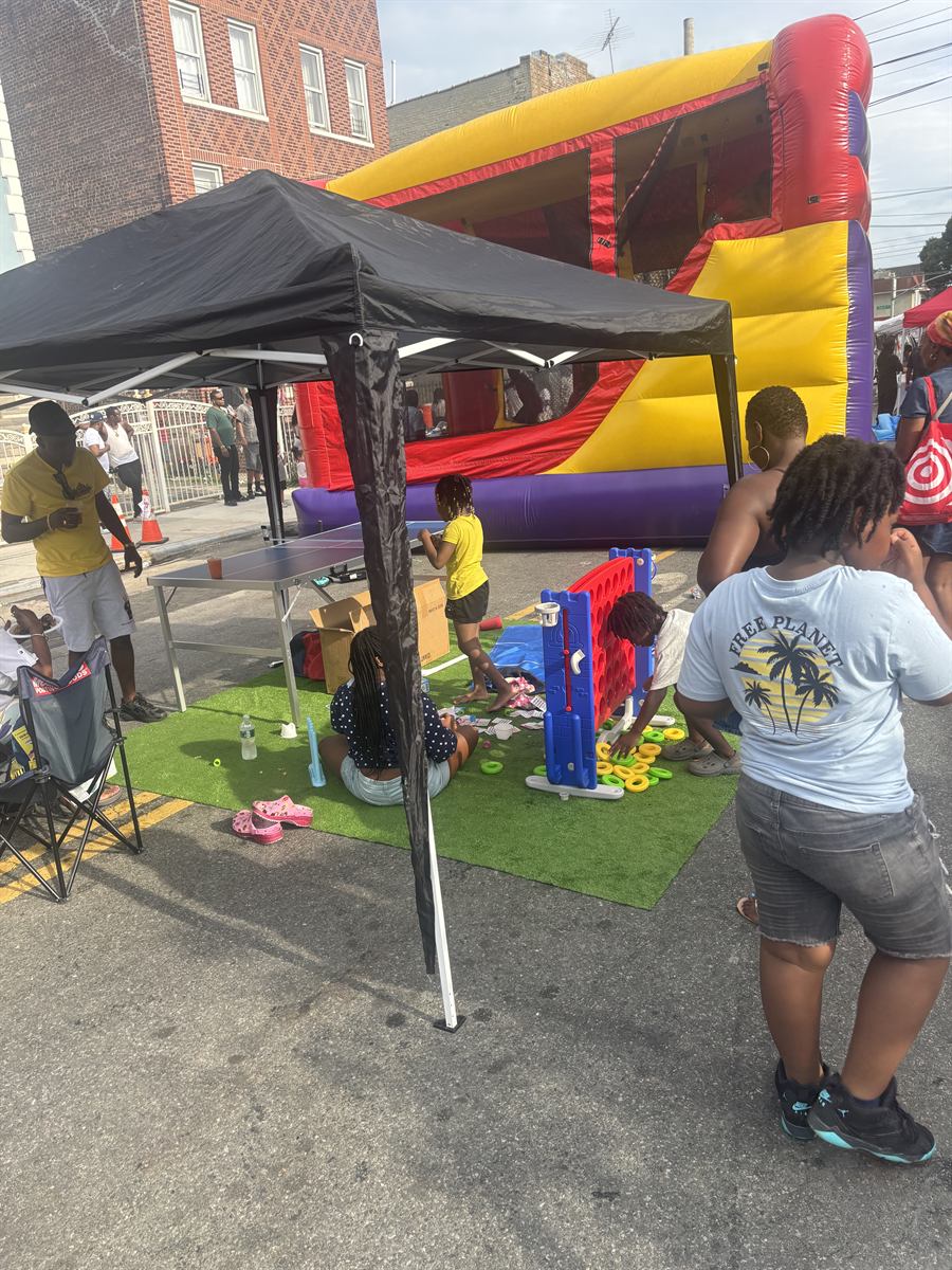 Kids playing giant Connect Four and ring toss on a patch of turf under a canopy, with an inflatable slide behind them