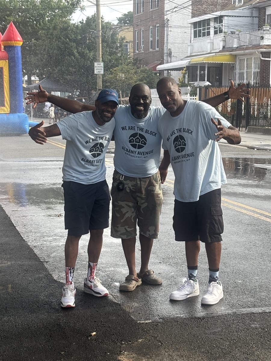 The three organizers in We Are The Block t-shirts, arms out, standing together in the middle of the closed avenue