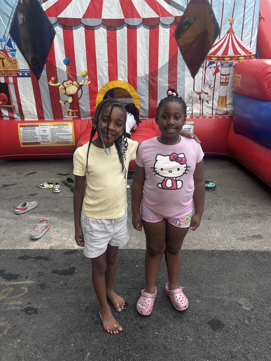 Two girls smiling in front of the bouncy house, shoes kicked off at the door