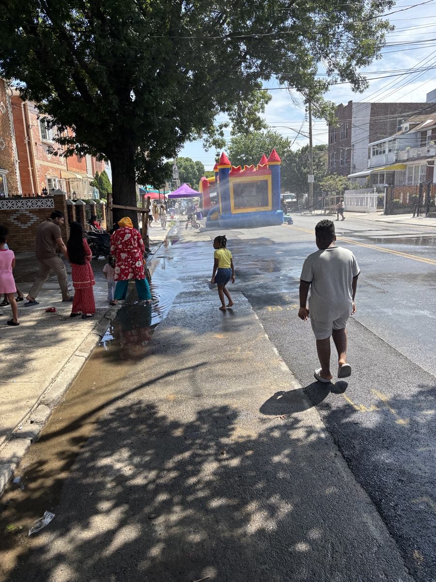 Kids playing in water from an open hydrant running down the closed street, with a bouncy castle at the far end